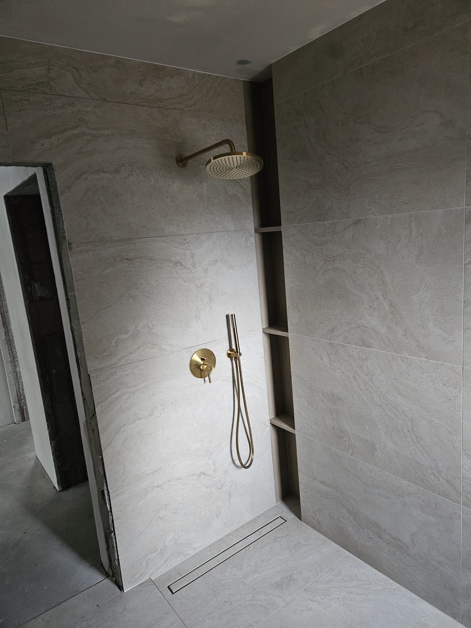 Prysznic walk-in z płytkami w ciepłym kamiennym wzorze, pionową wnęką i złotą deszczownicą