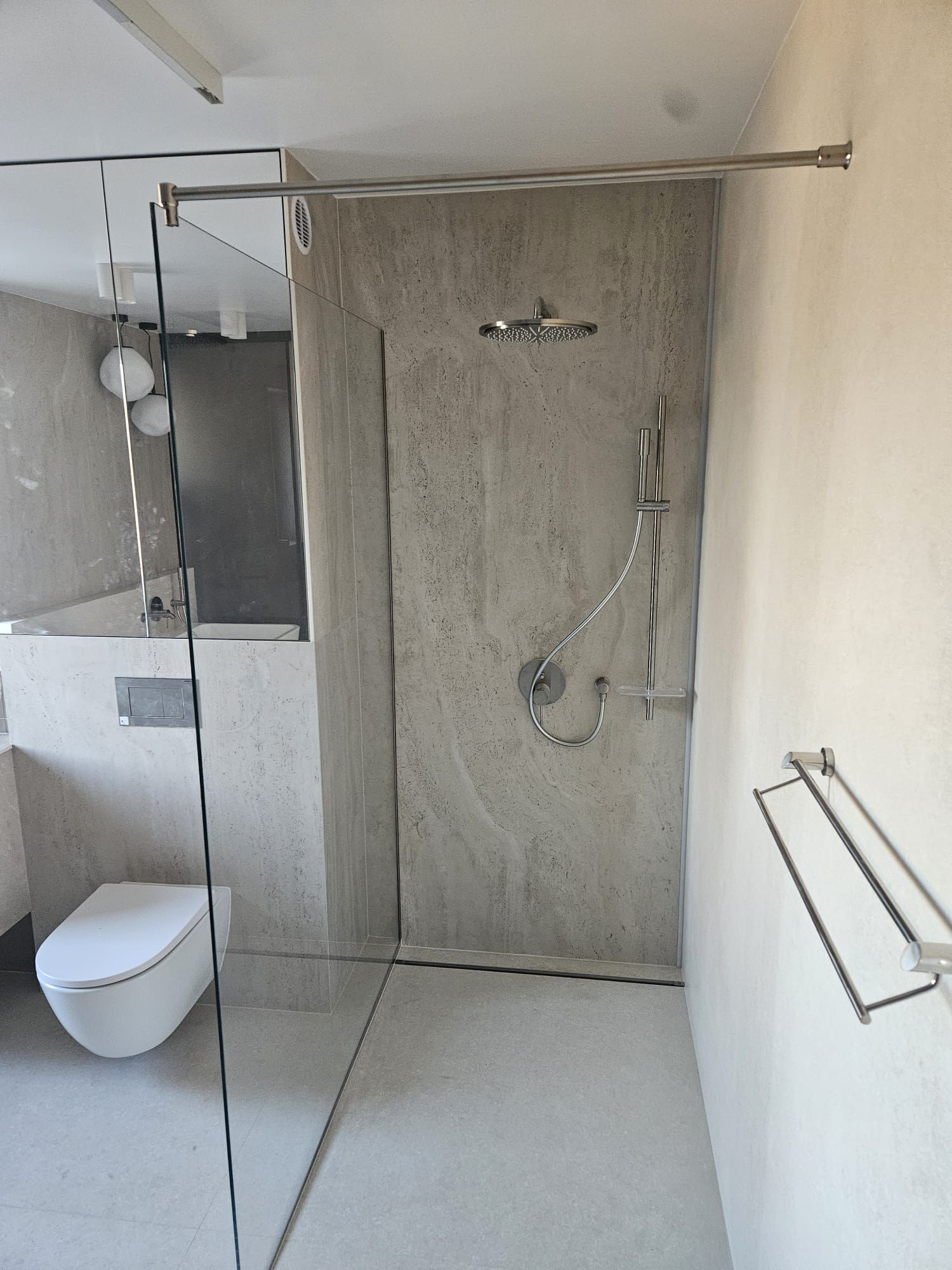 Prysznic walk-in z płytą w wzorze trawertynu, odpływem liniowym i podwieszanym WC
